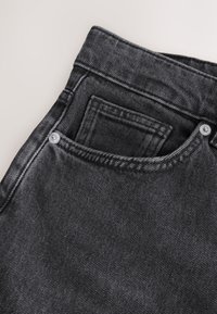 Close-up of black denim jeans waistband and front pocket with visible white rivets and detailed stitching.