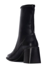 Bottine en cuir noir avec un design élégant et étroit, un talon block de taille moyenne et une finition lisse avec un minimum de détails de couture.