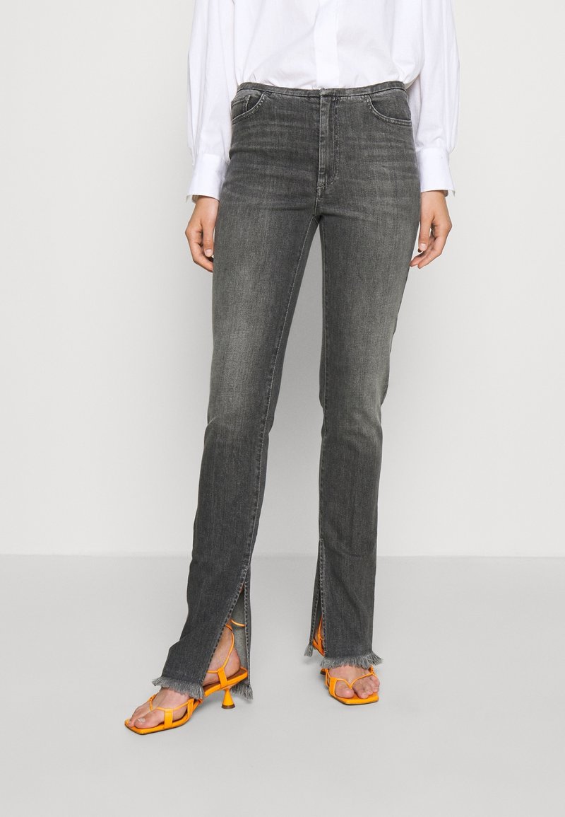 Gray denim jeans with split hems, featuring a fringed edge. Paired with orange strappy sandals. White button-up shirt in the background.