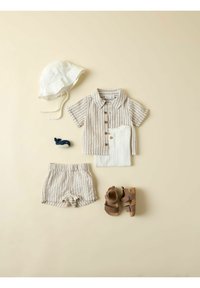 Tenue d'été pour tout-petit avec chemise beige à rayures manches courtes, short assorti, body blanc côtelé, chapeau blanc de soleil, sandales marron et petit jouet baleine.