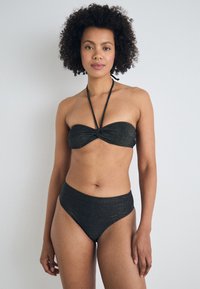 Črni bandeau bikini s zasukanjem spredaj in z zavezanjem na vratu. Visok pas na dnu, bleščeča tekstura in gladka tkanina.