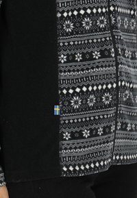 Giacca a zip in pile nera con pannello frontale decorato in bianco e grigio, dotata di un piccolo dettaglio a bandiera blu e gialla sul lato.