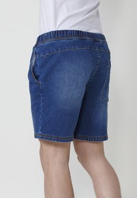 Tumši zili džinsu šorti ar elastīgu jostasvietu, sānu kabatām un aizmugures kabatu. Iezīmējās redzami šuvumi ap malām.