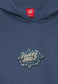 Mörkblå hoodie med en grafisk logotyp i ljusblått och vitt, med en textur på grafiken, tillverkad av mjukt bomullsmaterial.