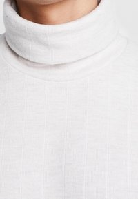 Biały prążkowany sweter z golfem, z wysokim, złożonym kołnierzem o miękkiej fakturze. Tkanina ma subtelne pionowe linie.