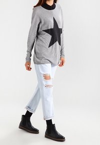 Szary sweter z czarnym wzorem gwiazdy, zestawiony z jasnoniebieskimi przetartymi dżinsami i czarnymi botkami za kostkę. Mi�ękka tkanina, luźny krój i kontrastowe warstwy.