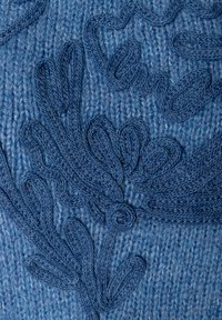 Blauer Strickstoff mit einem texturierten Blumenmuster, das schwungvolle Muster und einen auffälligen Spiralakzent aufweist, alles in verschiedenen Blautönen.