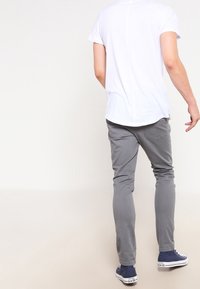 Šedé slim-fit kalhoty z bavlny s hladkou texturou. Nosené s bílým tričkem s jednoduchým designem a modrými teniskami.