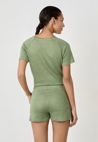 Zielony top z krótkim rękawem w luźnym fasonie i rękawami raglanowymi, połączony z dopasowanymi szortami z elastycznym pasem, wykonanymi z miękkiego materiału.