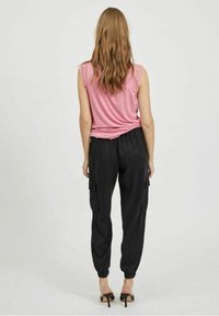 Rosa linne utan ärmar med spetsdetaljer vid axlarna, kombinerat med svarta cargobyxor med elastiska mudd och sidofickor. Höga svarta skor.