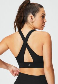 Zwarte sportbeha met een crisscross-ontwerp op de rug en een logoband. Gemaakt van rekbaar materiaal, met een gladde textuur en minimale naden.