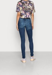 Vaqueros skinny de color azul oscuro con una textura suave, combinados con una camisa corta de estampado floral colorido. Un atuendo casual con zapatillas ligeras.