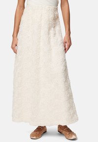 Jupe maxi blanche en tissu texturé avec un motif de roses, accompagnée de ballerines marron clair avec des accents en nœud.