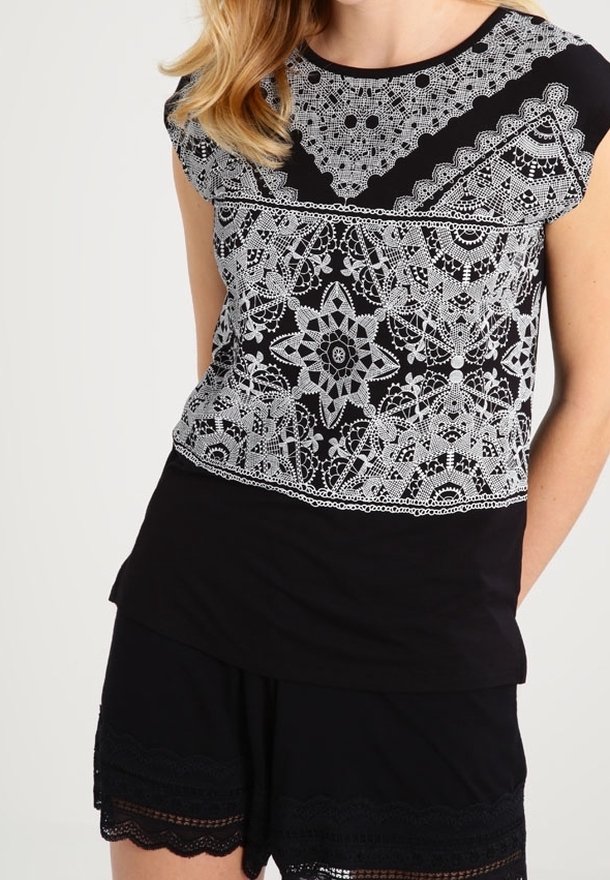 Schwarzes T-Shirt mit komplizierten, weißen Spitzenmustern im oberen Bereich und einem einfarbig schwarzen unteren Abschnitt. Kurze Ärmel und runder Ausschnitt.