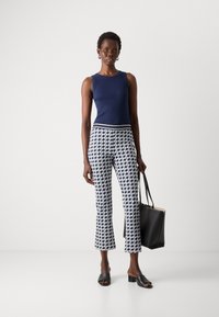 Marineblauw geribd tanktop, gepatternde zwart-witte cropped broek met een tailleband, zwarte open-toe mules, en een zwarte tote bag.