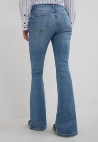 Hellblaue, ausgestellte Jeans mit mittelhoher Taille, die über genähte Taschen, eine glatte Denim-Textur und dezente Ausbleichungen an den Beinen verfügt.