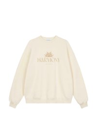 Sweatshirt couleur crème en tissu doux, avec un col rond, des manches longues et un graphique central de soleil avec le texte « HARMONY ». 
