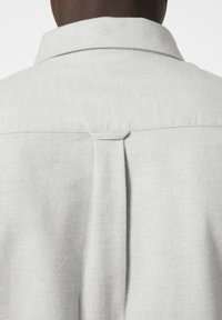 Camisa gris claro con cuello extendido, pliegue en la parte posterior y textura suave. Diseño simple sin patrones ni acentos visibles.
