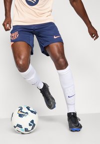 Navy and orange Nike shorts with FC Barcelona logo, white soccer socks, and black cleats. A patterned soccer ball is in the foreground.