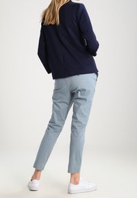 Námornická strukturovaná sako, světle modré pohodlné kalhoty a bílé tenisky. Sako má jednoduchý design, zatímco kalhoty mají klasický střih s ohrnutými manžetami.