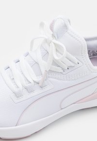 Zapatilla deportiva blanca con cordones texturizados atados en un lazo, parte superior de tejido de punto y una franja de acento rosa claro en la suela y el panel lateral.