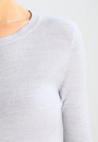 Jasnoszary sweter z długim rękawem i okrągłym dekoltem. Miękka, wełniana w dotyku tekstura i gładkie wykończenie bez widocznych wzorów czy elementów metalowych.