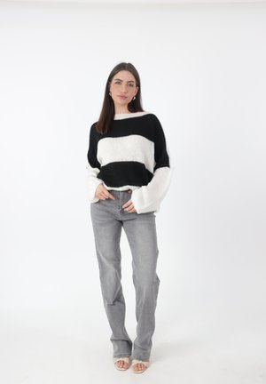 Zwart-wit gestreepte gebreide trui met brede mouwen, gecombineerd met lichtgrijze rechte jeans en nude sandalen op een effen achtergrond.
