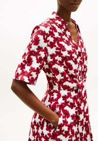 Vestito floreale con scollo con colletto, maniche corte, motivo a fiori rossi su sfondo bianco e accentuazione in vita con nodo e tasche.