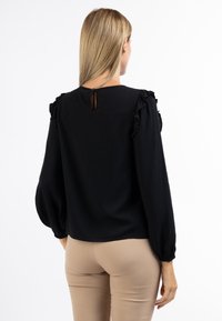 Blusa nera con spalle arricciate, schiena a chiave e maniche lunghe a palloncino. Realizzata in tessuto texturizzato con una vestibilità rilassata.