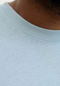 Lyseblå T-shirt med rund halsudskæring. Materialet virker blødt med en glat tekstur og subtil syning langs kraven.