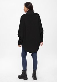 Poncho nero a coste con alto collo, maniche ampie e vestibilità comoda, abbinato a jeans blu e stivali neri stringati.