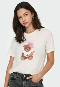Hvid t-shirt med korte ærmer, der viser en tegneserie bjørn med en lyserød beret, der holder en baguette, samt et grafik af Eiffeltårnet.