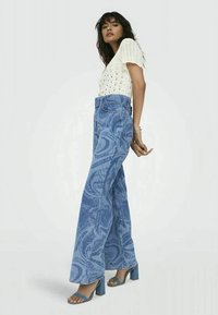 Top leggero in maglia crema con maniche corte a sbuffo abbinato a jeans a campana a vita alta con motivo marmorizzato blu e sandali con tacco blu.