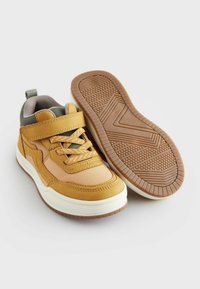 Geel en tan sportieve schoenen met een gepolsterde kraag, veters en klittenbandsluitingen, en een getextureerde rubberen zool voor grip en stabiliteit.
