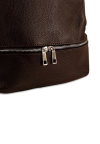 Bruine leren tas met een gestructureerd oppervlak, metalen ritsen en contrasterende stiksels. Het ontwerp heeft een opvallend ritsdetail aan de onderkant.