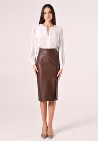 Weiße Bluse mit langen Ärmeln und einer Knopfleiste, kombiniert mit einem braunen Leder-Bleistiftrock mit hoher Taille und einem seitlichen Schlitz.