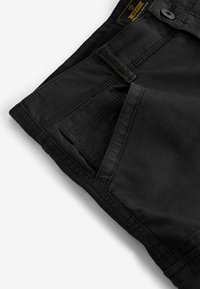 Sorte shorts med glat front, der har en enkelt lomme på højre side, synlige syninger og en blød, mat tekstur.