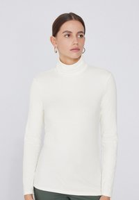 Top de cuello alto color crema con mangas largas, realizado en una tela suave y liviana. Presenta un diseño ajustado y un estilo minimalista.