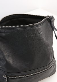 Borsa secchiello in pelle nera con superficie testurizzata, chiusura con zip e tasca esterna con cerniera alla base. L'interno è foderato in tessuto nero.