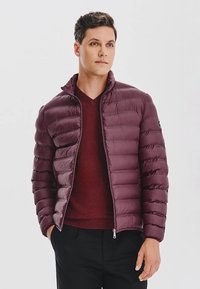 Bordowa kurtka puchowa z kołnierzem z przeszyciem w poziomie i zapięciem na zamek, w komplecie z bordowym swetrem z dekoltem w serek.