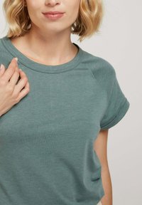 T-shirt à manches courtes, col rond, dans une couleur verte muted. Fabriqué en tissu doux et extensible avec une texture subtile et un design de manches raglan.