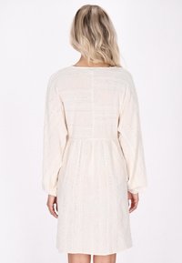 Rochie de culoare crem, cu mâneci lungi, din stofă texturată și dungi verticale, având detalii brodate subtile pe spate.