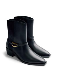 Botas de cuero negro hasta la mitad de la pantorrilla con punteras afiladas, tacones bajos en bloque y detalle de correa con hebilla dorada sobre fondo blanco.