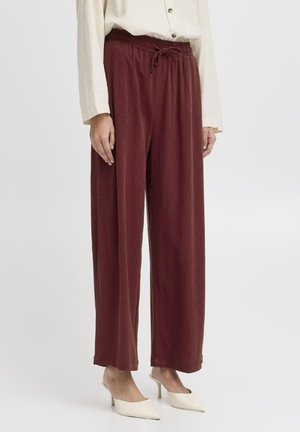 Pantalons larges bordeaux en tissu doux avec une taille élastique et un cordon de serrage ajustable. Associés à des mules crème.