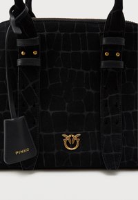 Musta mokkanahkainen käsilaukku krokotiilinkuosisella pinnalla, kultaisilla yksityiskohdilla ja koristeellisella logolla. Varustettu lyhyillä kahvoilla ja vetoketjullisella sulkemisella.