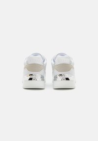 Sneaker bianchi con accenti argento, dettagli testurizzati e un tacco liscio e lucido. Il nome del brand "GUESS" è impresso sul retro.