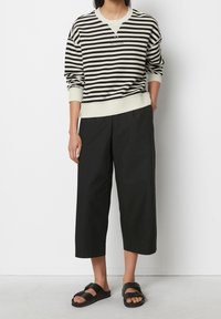 Felpa a righe nera e crema con collo a giro, abbinata a pantaloni cropped neri larghi e sandali neri. Design semplice e rilassato.