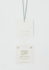 Metki odzieżowe z napisem "DOŁĄCZ DO ŻYCIA" i "Dbaj o włókna", wskazujące na co najmniej 50% ekologicznej bawełny, wykonane w 100% z recyklingowanego papieru, przymocowane zieloną nitką.