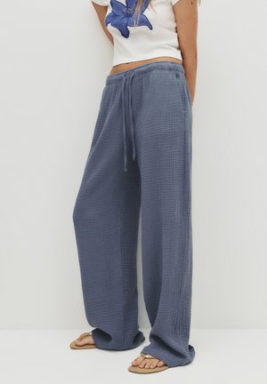 Pantalons légers à jambe large en tissu bleu texturé, avec une taille élastique et un cordon de serrage, associés à un haut blanc à fleurs court.