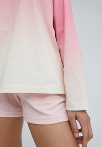 Kevyt, liukuvärjätty rentoutumisasu, joka sisältää pitkähihnaisen paidan, joka haalistuu vaaleanpunaisesta valkoiseen, sekä pehmeät, vaaleanpunaiset froteeshortsit, jotka ovat rennon malliset.